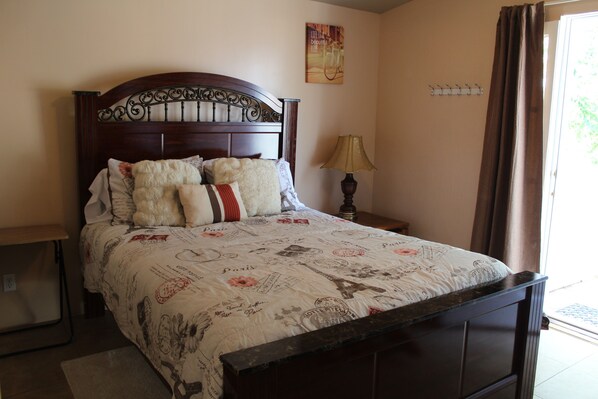 habitación de la entrada, cama tamaño Reina, silla, mesa y tv.