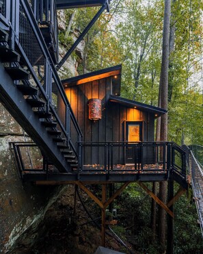 Front facade of Sandstone Drifter nestled under sandstone ledge – bold, bandit‑hideout inspired architecture with large rock overhang, encapsulating the rugged Red River Gorge cliff dwelling experience.