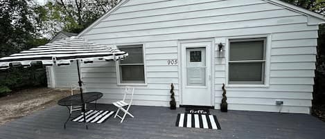 Front of home features an outside deck with table, chairs and umbrella.