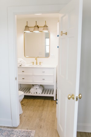 Enjoy a bright, modern ensuite bathroom featuring brass fixtures, fresh towels, and a spacious vanity. Clean, comfortable, and thoughtfully designed—perfect for relaxing after a day exploring the charm of Boothbay Harbor.