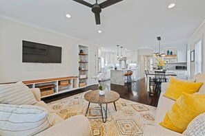 Living Room with built in shelving, ceiling fan, queen pull out couch and TV Open to Kitchen/Dining area