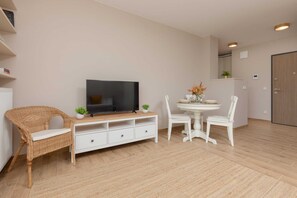 A cozy living room with a light-colored sofa, a small dining table, and large windows that bring in natural light, creating a welcoming atmosphere.