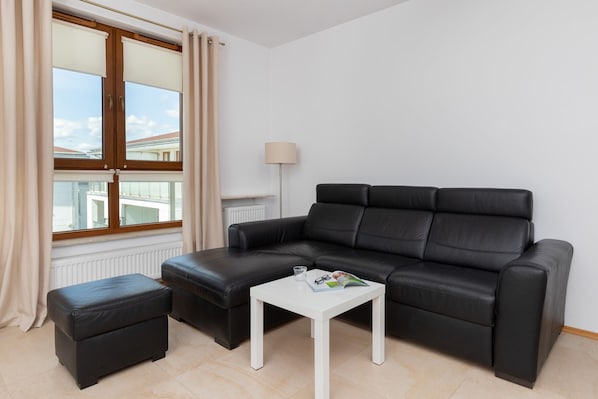 A bright and open living area with a modern black leather sofa, coffee table, and large windows that allow natural light to fill the room.