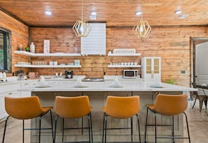 Stylish kitchen with white countertops, wooden wall panels, and mustard-colored bar stools, illuminated by unique geometric lights