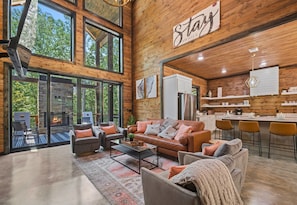 A beautiful interior of a modern home with towering windows, a wooden ceiling, a comfortable living area, and a kitchen with bar stools