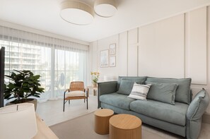 A bright living room with a modern design, featuring a comfortable gray sofa and large windows overlooking greenery.