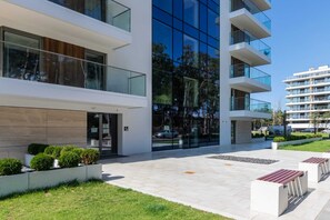 The entrance of the building is surrounded by manicured greenery and a clean, modern architectural design.
