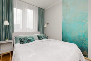 A serene bedroom featuring a double bed with teal accents, a decorative feature wall, and natural light for a welcoming ambiance.

