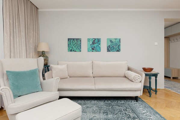 A bright and cozy living room with a white sofa, turquoise cushions, and modern artwork, creating a relaxing and stylish space.


