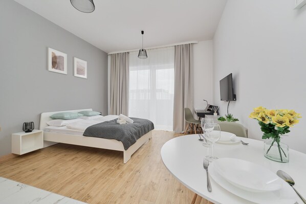 A bright and airy studio apartment with a neatly made bed, wooden furniture, and soft lighting for a welcoming ambiance.