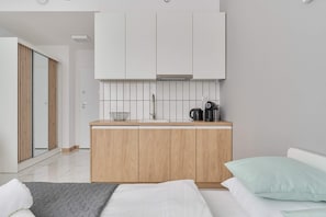 A compact kitchenette featuring sleek white cabinets, wooden accents, and essential appliances for convenient cooking.