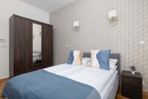 A serene bedroom showcasing a double bed with a blue headboard, crisp white bedding, and soft blue accent pillows. 