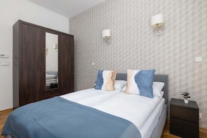 A serene bedroom showcasing a double bed with a blue headboard, crisp white bedding, and soft blue accent pillows.