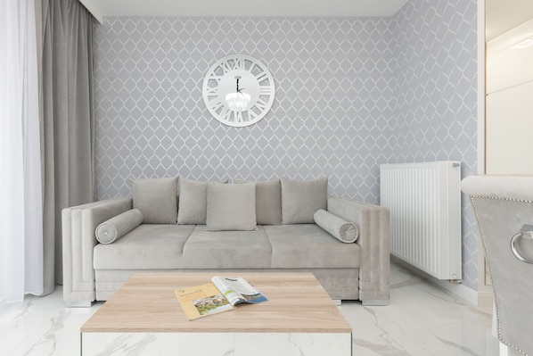 A bright and stylish living room featuring a modern gray sofa, a wooden coffee table, and elegant decor with a large wall clock.