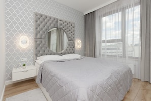 A cozy bedroom with a plush gray bed, quilted headboard, and a circular mirror, creating a sophisticated ambiance.