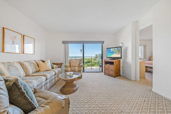 Bright and spacious living room with cozy seating and a TV, leading to a balcony.