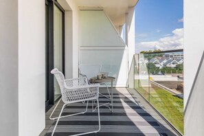 A private balcony with white wicker chairs and a modern rug, overlooking a green and peaceful area.

