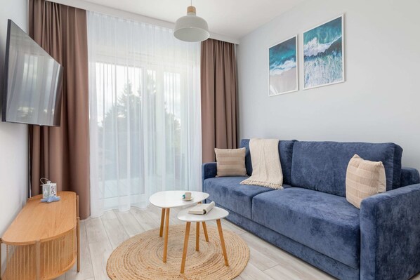 A cozy living room featuring a navy blue sofa, a round wooden coffee table, and large windows bringing in natural light.

