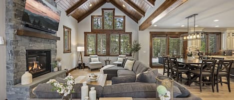 This living room is a vision of rustic elegance, featuring a towering stone fireplace, plush seating, and natural wood beams
