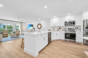 There are 5 sky-blue rattan bar stools at the impressively large quartz kitchen counter. The kitchen also has a kitchen nook with 2 upholstered rattan and cane benches, a modern contemporary white round table, and a decorative Fiddle tree.