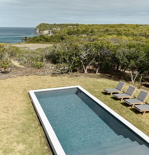 Panoramic Pool View from Seaside Villa on the Mountain in Marie Galante, with Comfortable Wooden Sunbeds and Cliffs in the Background