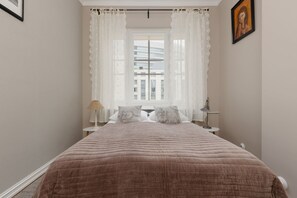 A bright bedroom featuring a double bed with soft bedding and a window allowing natural light.

