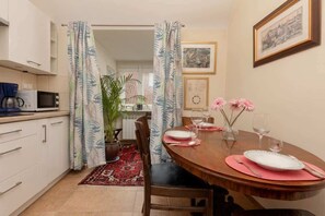 A compact dining area with a wooden table, colorful curtains, and a kitchenette in the background.

