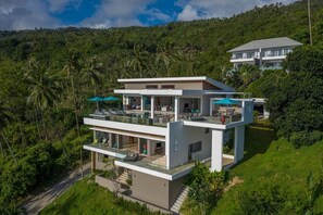 "Drone footage captures the villa's majestic exterior, surrounded by lush tropical greenery and stunning mountain views."