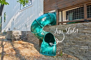 A unique green slide attached to the cabin provides a fun and quick descent, adding a playful element to the outdoor space.