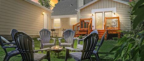 Quiet backyard w/ 8 fire pit chairs, bag toss, deck, patio furniture, and charcoal grill.