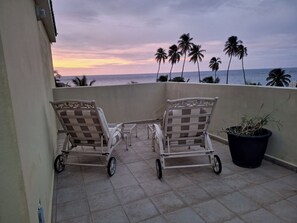 1 part of roof deck with two lounge chairs, and views of ocean, palms and sunset