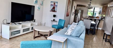Large living room, sleep sofa and 65” 4K TV with dining room in the background.