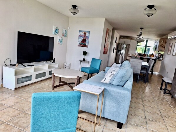 Large living room, sleep sofa and 65” 4K TV with dining room in the background.
