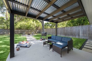 Backyard with grill, comfy sitting area, and cornhole set.