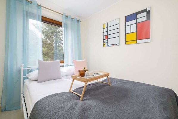 A bright and cozy living area with a gray sofa, light curtains, and colorful modern wall art.

