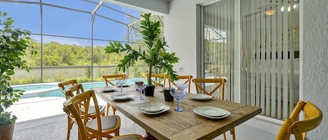 This inviting dining area is bathed in beautiful natural light, creating a warm and welcoming atmosphere. The view of the pool in front adds a touch of serenity to the setting, making it a perfect spot to enjoy a meal in harmony with nature.