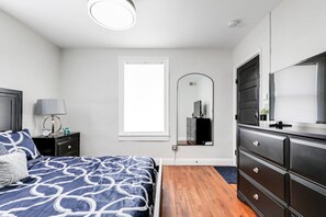 Primary bedroom with natural light, plush queen sized bed, dresser storage, flat screen Roku TV, remote controlled ceiling fan, full-length mirror and nightstand storage.