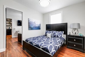 Primary bedroom with natural light, plush queen sized bed, dresser storage, flat screen Roku TV, remote controlled ceiling fan, full-length mirror and nightstand storage.