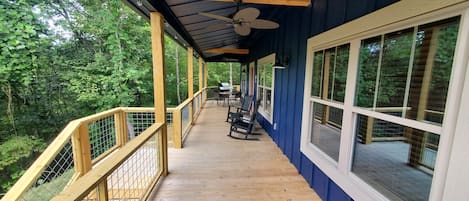 Front porch w/ grill, table, rocking chair, and overhead fans.