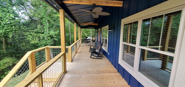 Front porch w/ grill, table, rocking chair, and overhead fans.