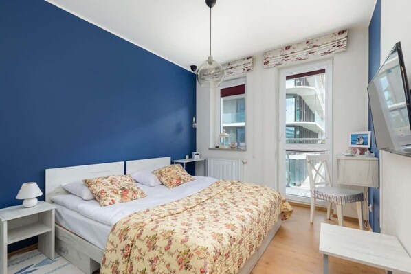 A comfortable bedroom with a blue accent wall, a double bed, and large windows offering plenty of light.
