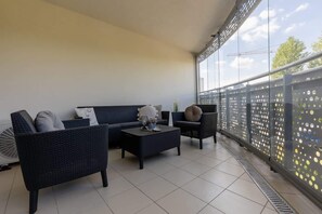 A large balcony with outdoor seating, including cushioned chairs and a table, offering a relaxing view.

