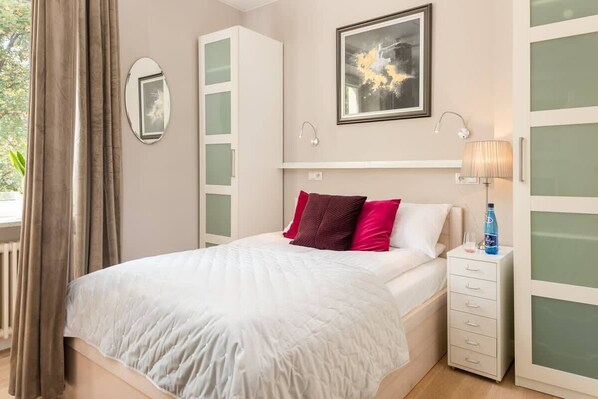 A cozy bedroom with a double bed, vibrant red and purple pillows, and soft lighting creating a warm atmosphere.

