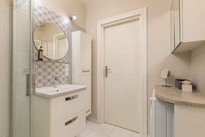 A compact and stylish bathroom with a walk-in shower, vanity, and mosaic tiles adding an elegant touch.