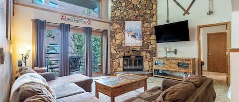 Living room with vaulted ceilings, floor-to-ceiling stone wood-burning fireplace, flatscreen Smart TV, and games.