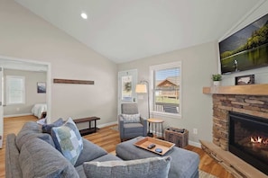 Unwind in the cozy living area featuring a comfortable sofa adorned with pillows, a stylish chair, a TV for entertainment, direct access to the outdoor deck, and the inviting warmth of an indoor fireplace.