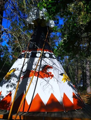 The Wild Horses Tipi is a large 20-footer set up on an oversized deck. It has four outdoor chairs, a large umbrella, a propane fire pit, a picnic table, and a briquet BBQ grill.