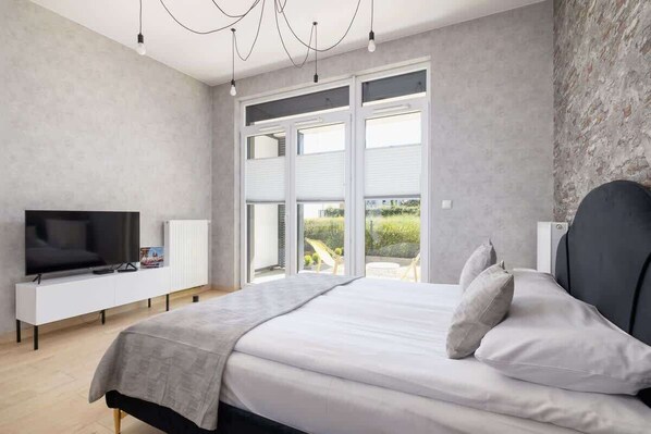 A bright and modern bedroom with a comfortable double bed, soft linens, and large windows allowing natural light to fill the space.

