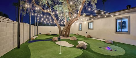 Miniature golf course lit up under cafe lights for nighttime playing