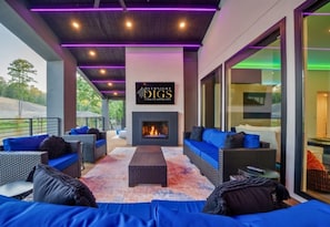 [Living Room] A stylish outdoor living space with a modern fireplace surrounded by comfortable seating with deep blue cushions and fluffy throw pillows